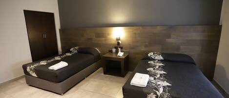 A hotel room with two single beds, a nightstand with a lamp, and a dark-colored wardrobe.