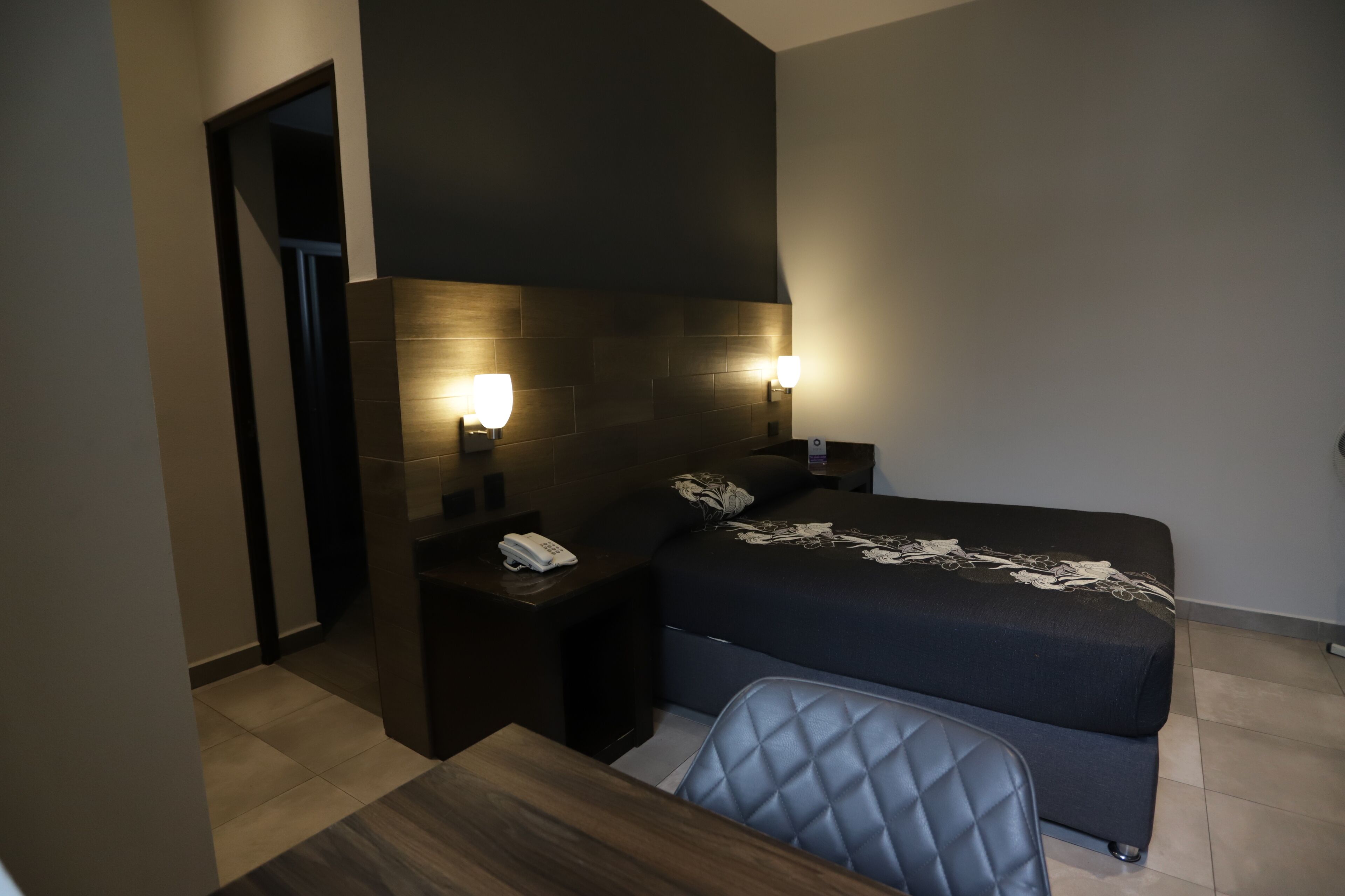 A hotel room with a bed, bedside tables, a desk, and a chair.