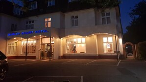 Hotel Burley Court, con una entrada bien iluminada y un área de estacionamiento al frente.