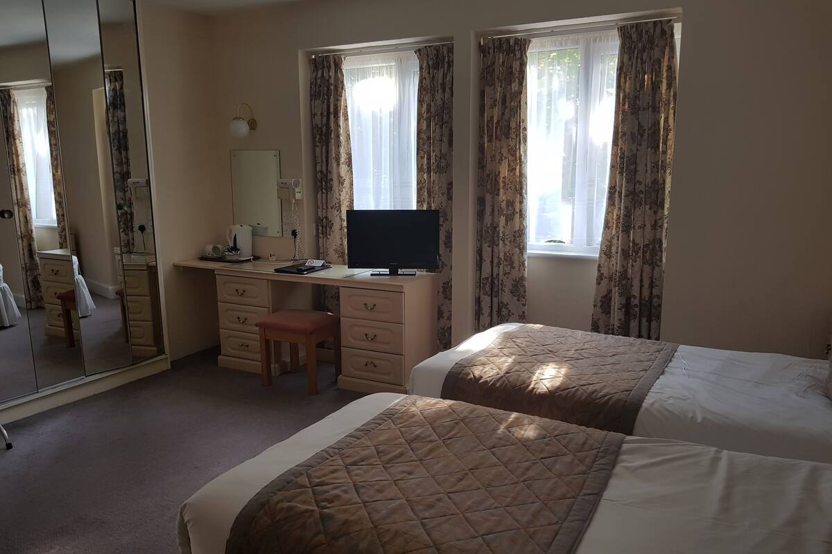 A hotel room with two beds, a desk with a computer, a mirror, and a dresser.