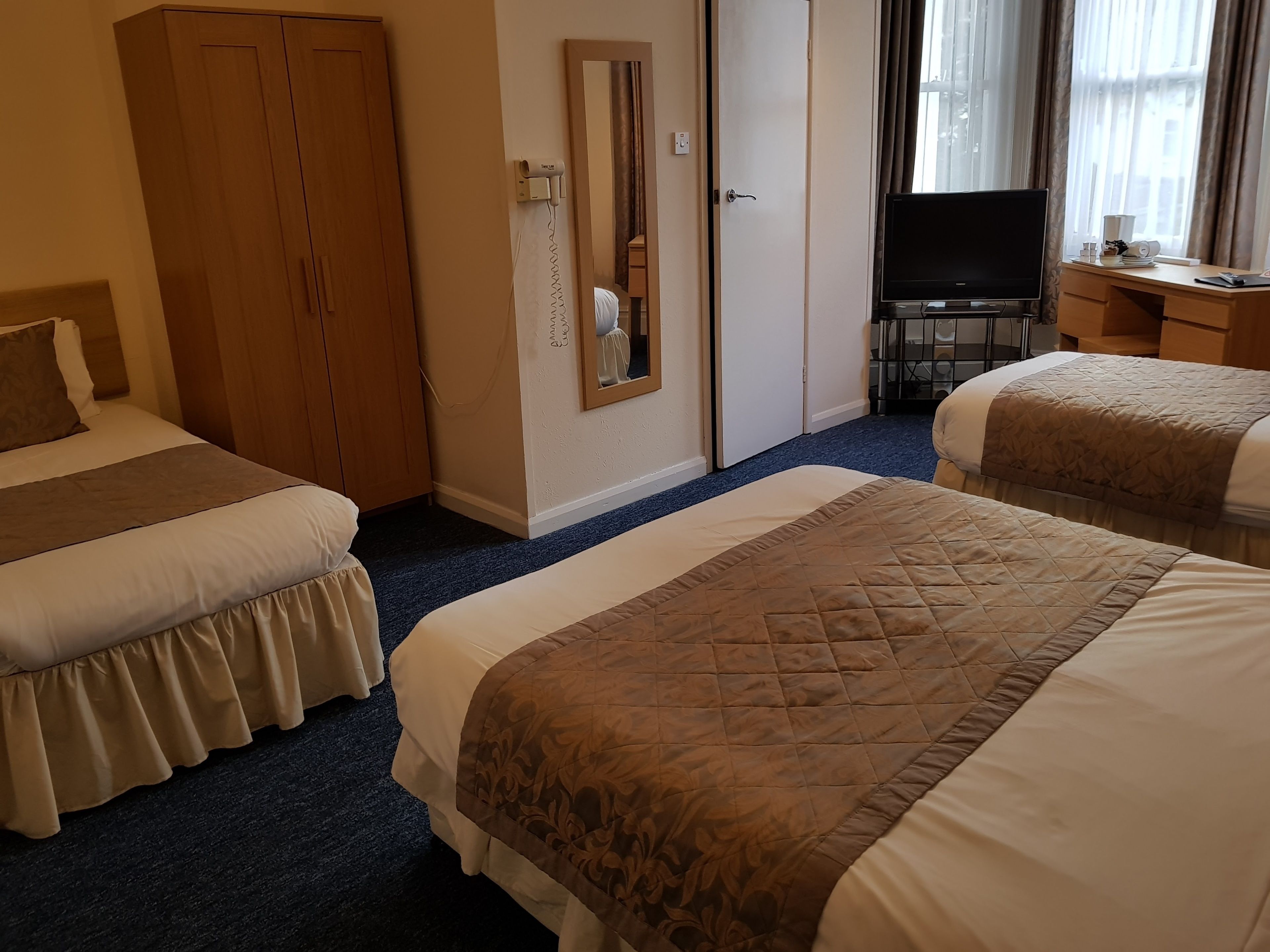 A hotel room with two beds, a wardrobe, a desk with a computer, and a TV.