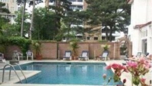 Piscina con sillas de descanso y un muro de ladrillo al fondo.