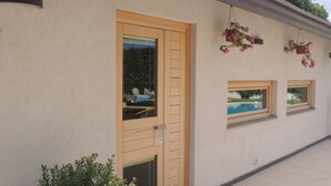 Un bâtiment à la façade beige, doté d’une porte en bois et de deux fenêtres donnant sur une piscine.