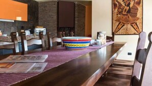 Un espace repas avec une longue table en bois, des chaises, un bol aux couleurs vives et un tableau accroché au mur.