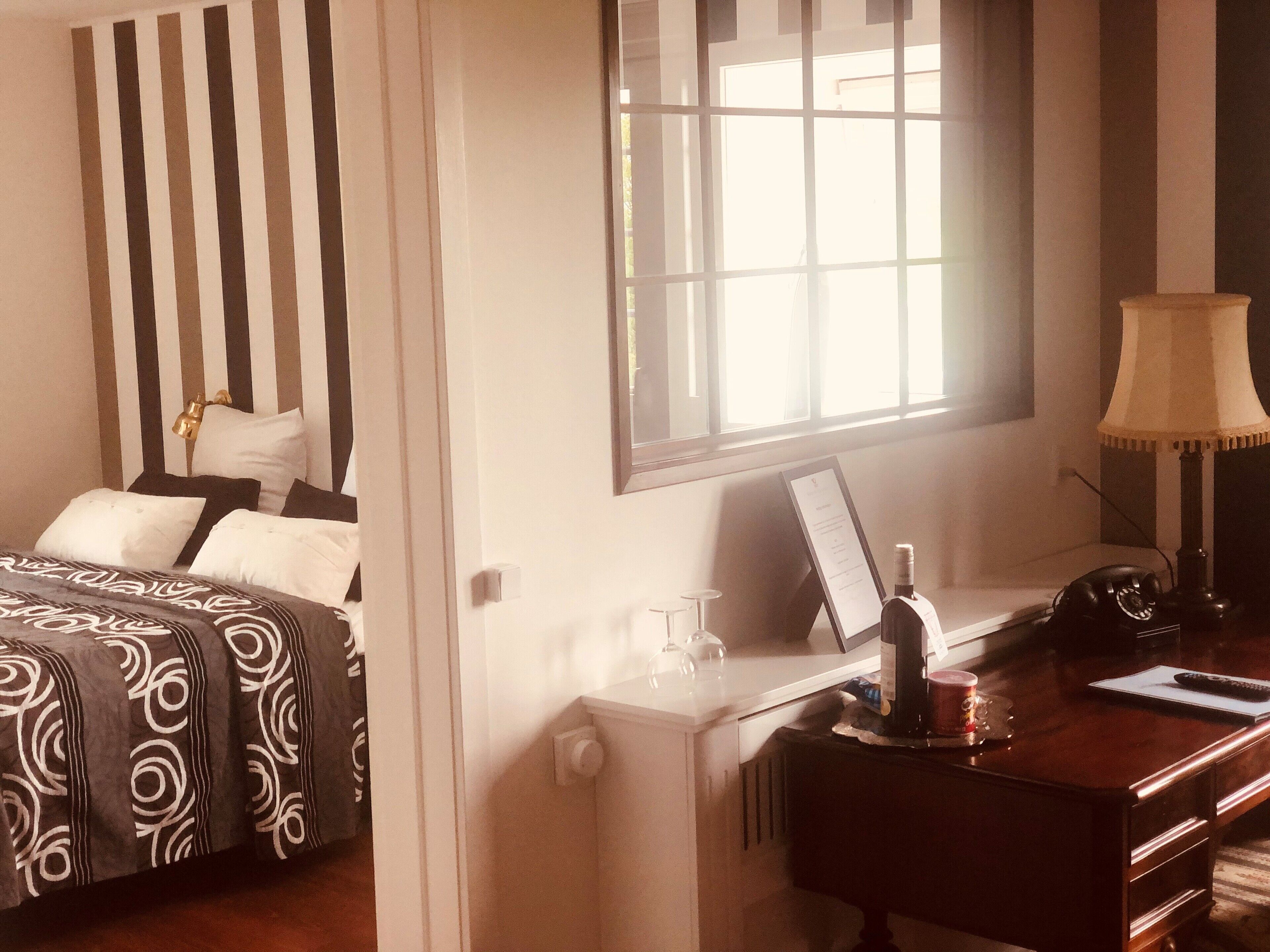 A hotel room with a bed, a desk with a lamp, a window, and a view of the outside.