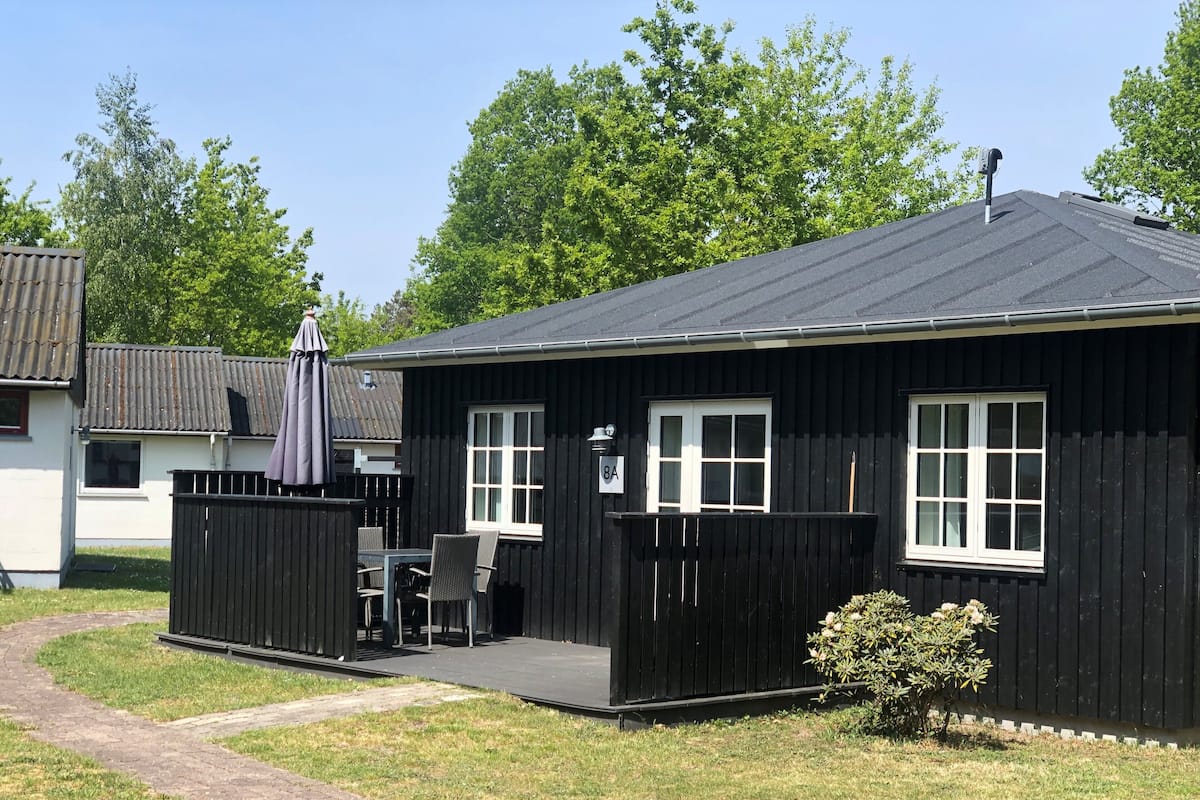A small black wooden building with a porch, a table, and chairs.