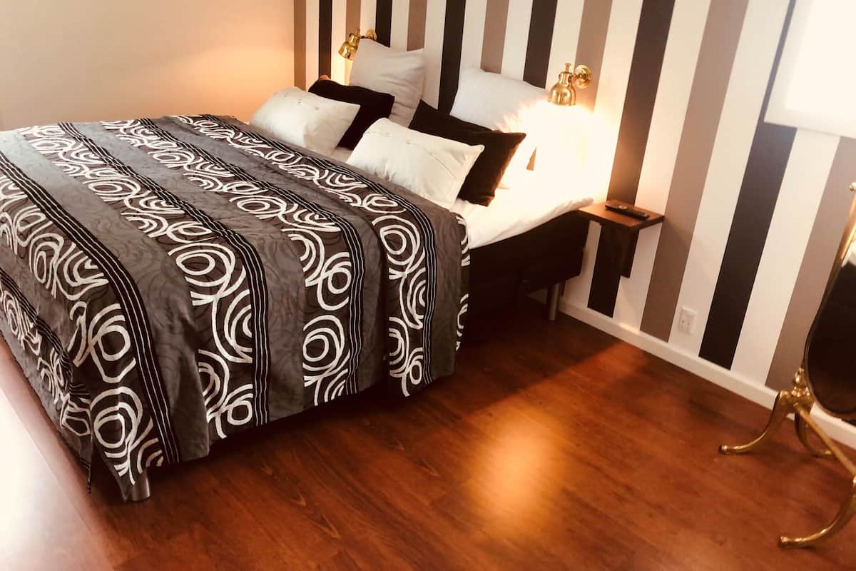 A bed with a patterned bedspread, a bedside table with a lamp, and a wall with vertical stripes.