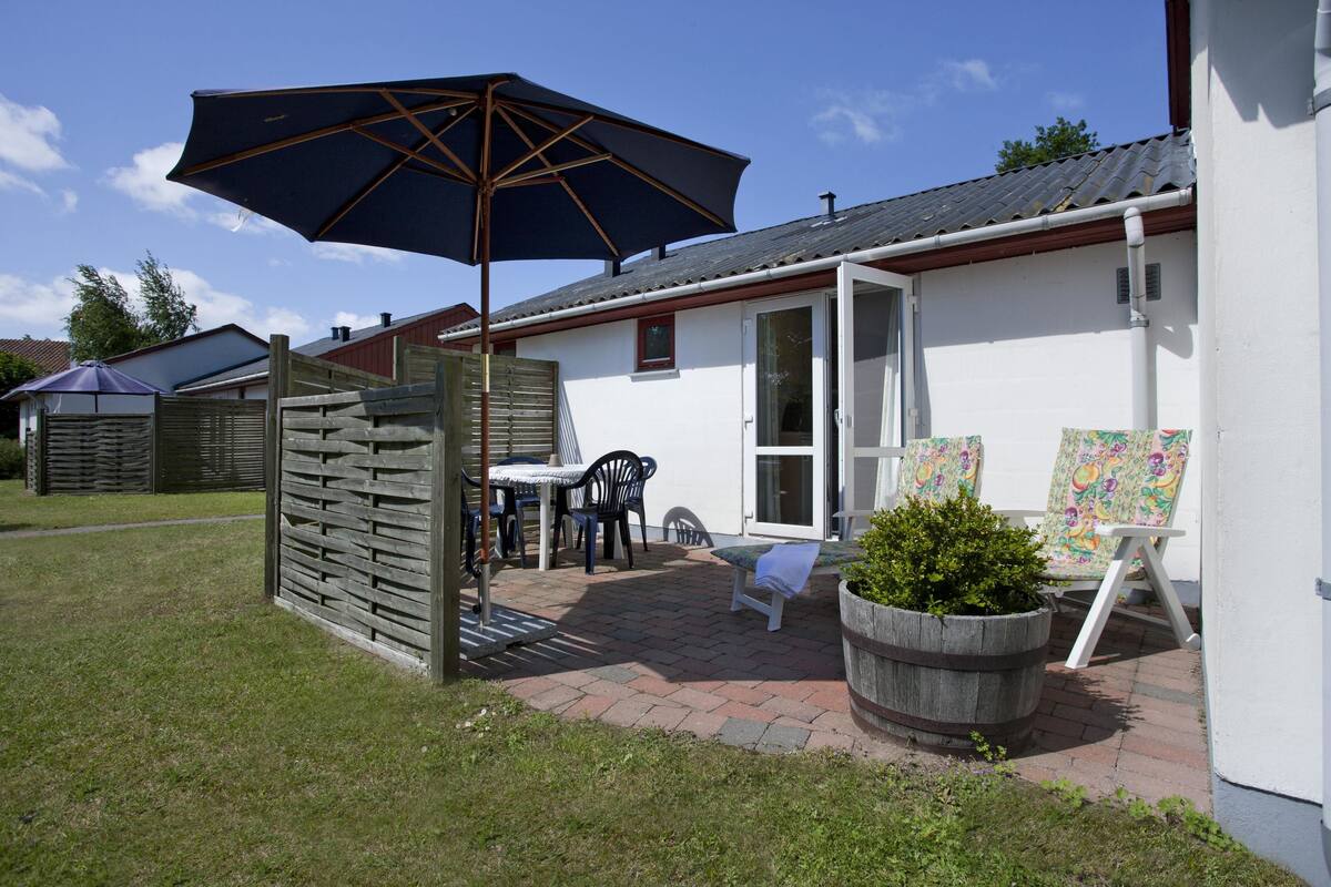 A patio with a table and chairs, a large umbrella, and a planter with greenery.