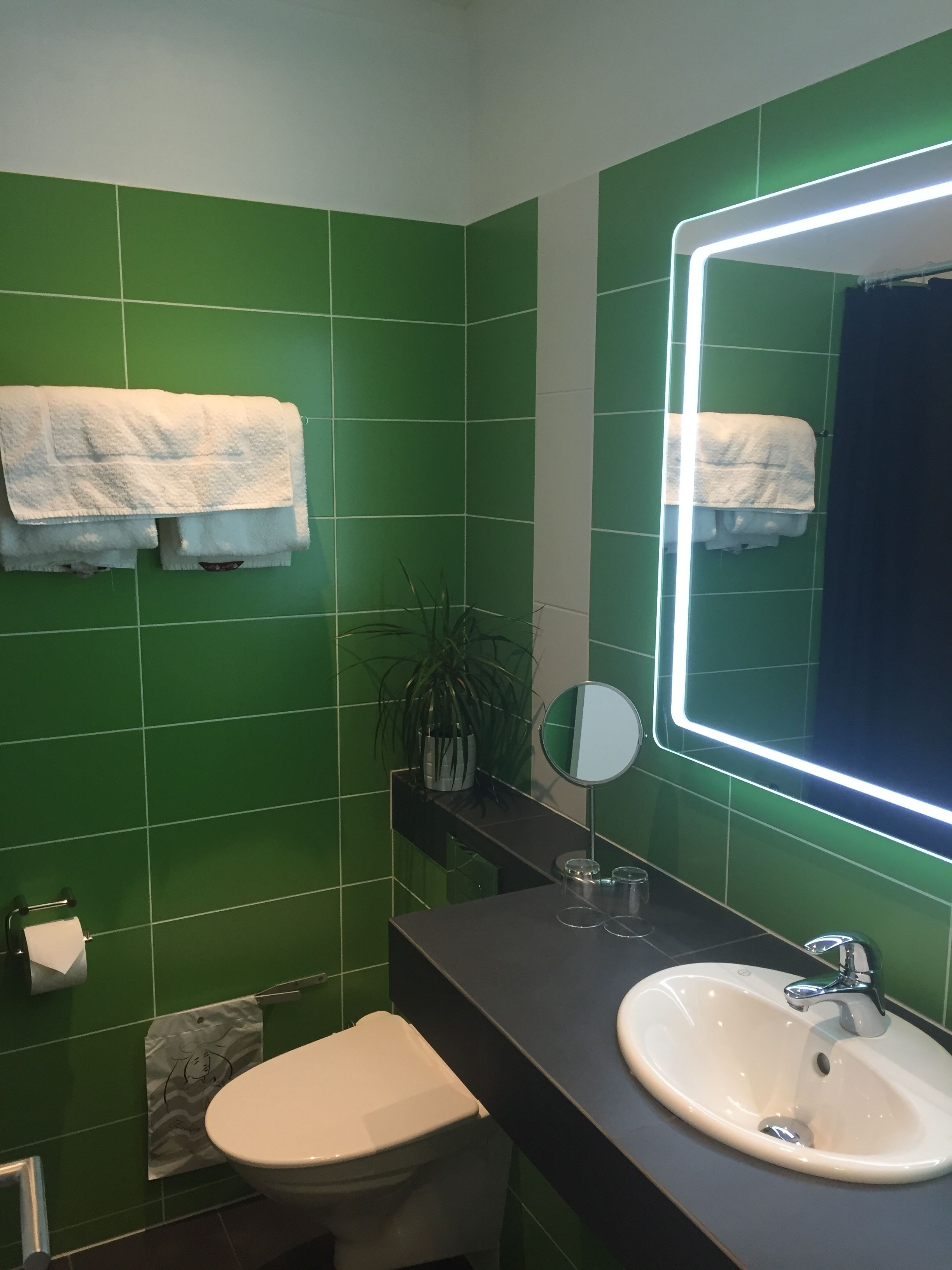 A bathroom with green tiles, a white sink, a mirror, and a toilet.