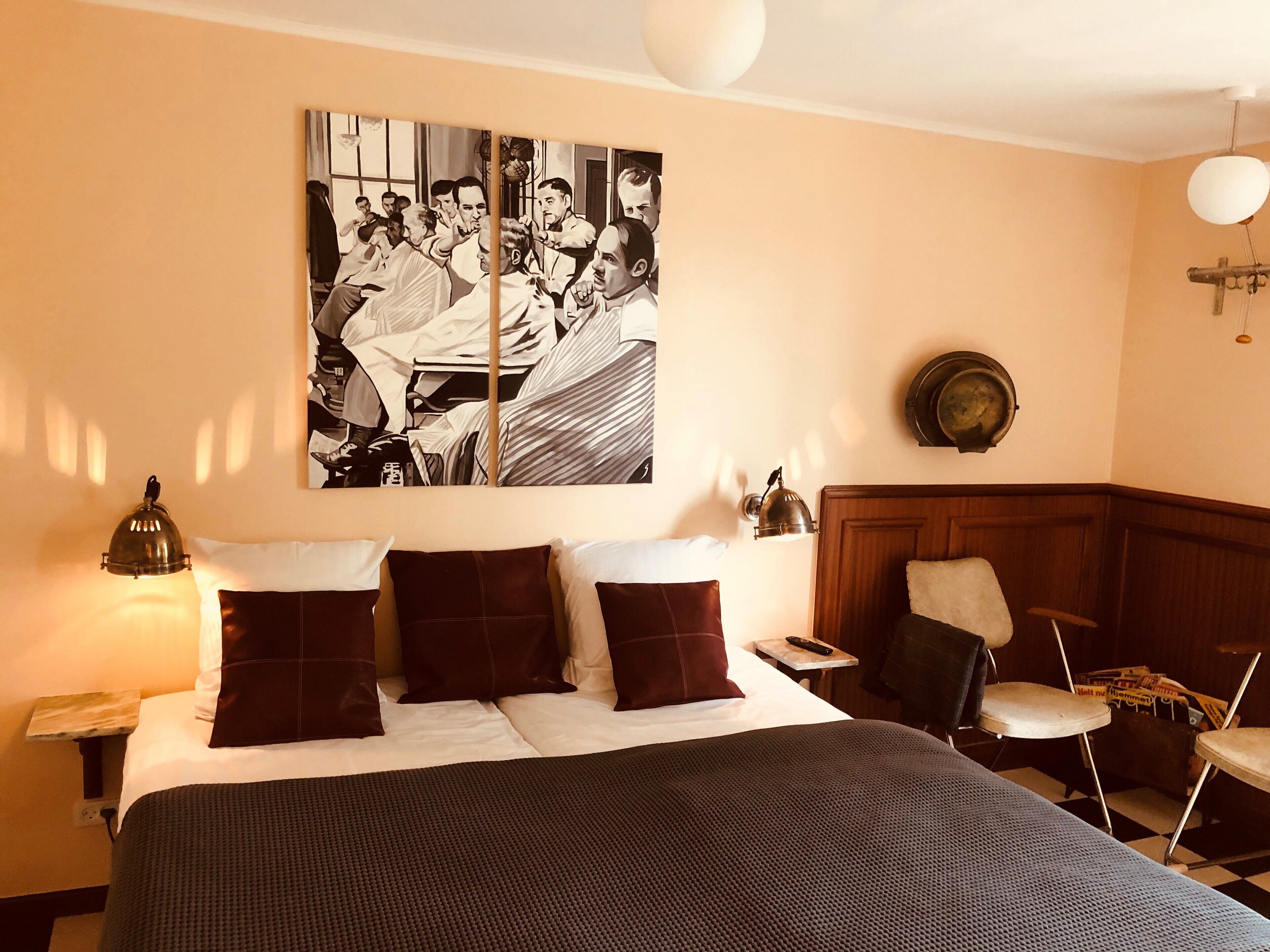 A hotel room with a large bed, a wooden headboard, a side table with a lamp, a chair, and a wall-mounted picture.
