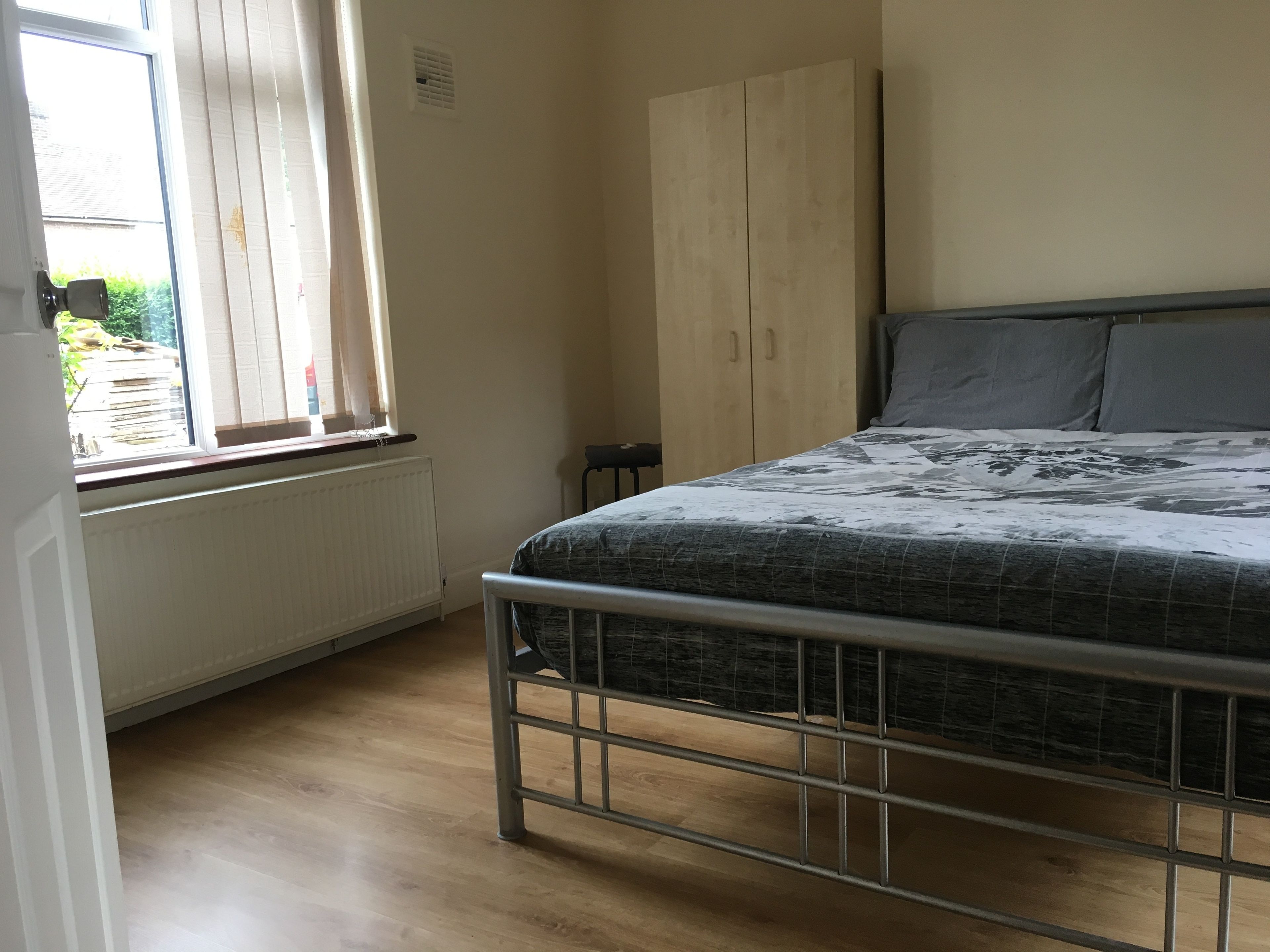 A bedroom with a metal bed frame, a window with blinds, a radiator, and a wardrobe.