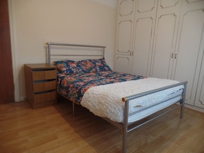 A single bed with a metal frame, a wooden nightstand, and a wardrobe with a white door. - Dawpool House (London)