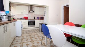 Cocina compacta con alacenas blancas, un refrigerador pequeño, un microondas y una estufa. Hay una mesa de comedor con sillas coloridas.