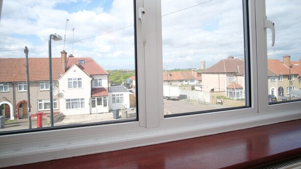 Una ventana con vistas a una zona residencial, con casas de tejados rojos y cielo despejado.