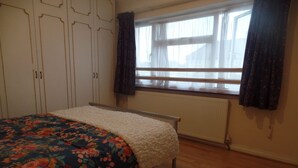 Un dormitorio con cama, ventana con cortinas, radiador y suelo de madera.
