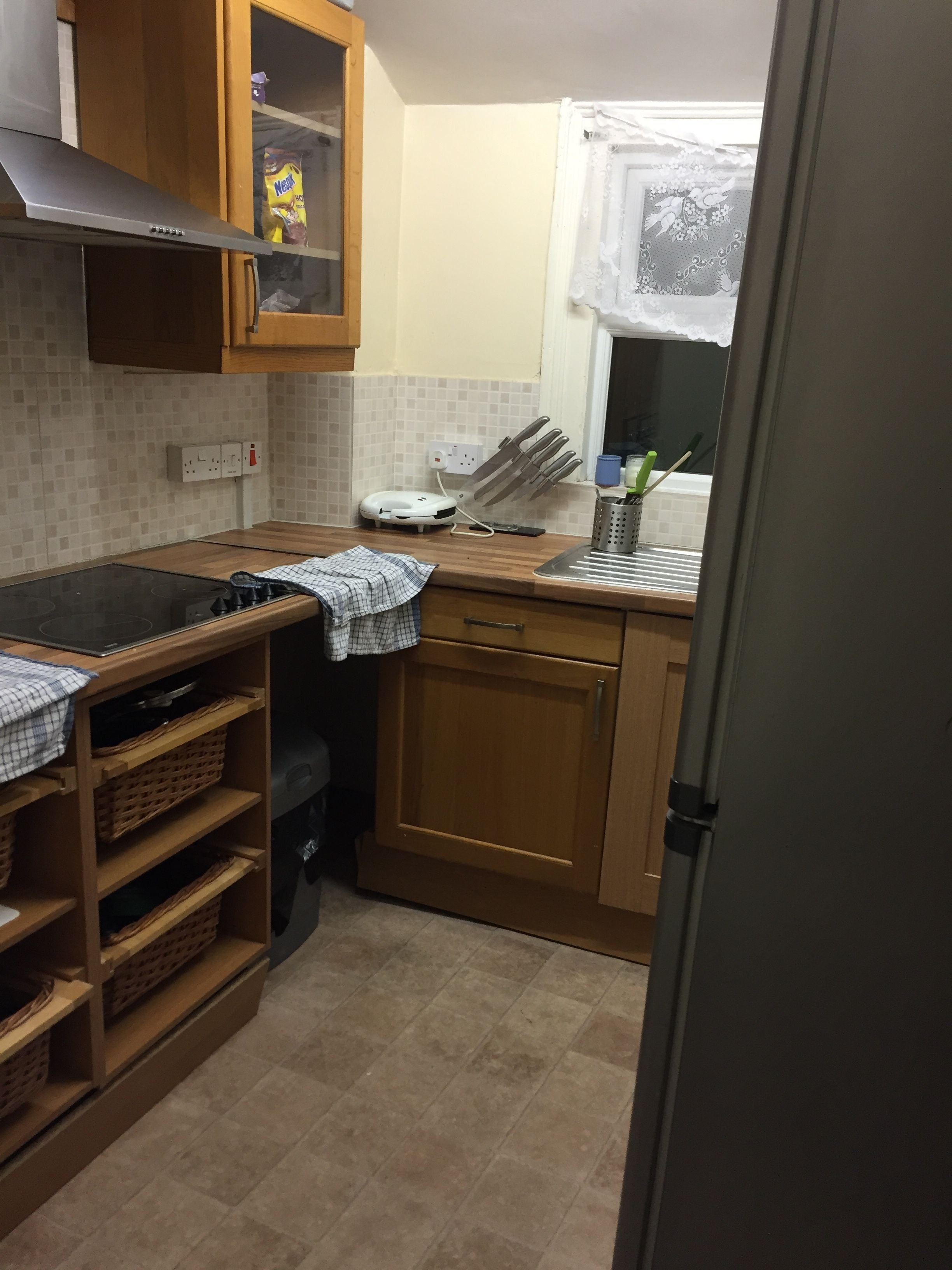 A compact kitchen with a gas stove, wooden cabinets, a microwave, and a window with a curtain.