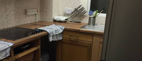 A compact kitchen with a gas stove, wooden cabinets, a microwave, and a window with a curtain.