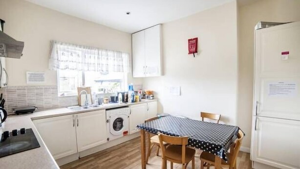 A compact kitchen with a washing machine, a sink, a table with chairs, and a refrigerator. - Harley House (London)