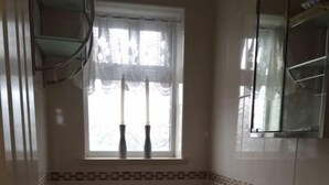 A bathroom with a toilet, sink, and window with a curtain. - Harley House (London)