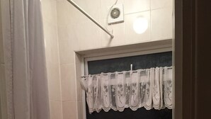 A bathroom with a bathtub, a sink, and a window with a lace curtain. - Harley House (London)