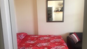A bedroom with a bed covered in a floral-patterned red bedspread, a dark-colored sofa with a striped pillow, and a mirror on the wall. - Harley House (London)