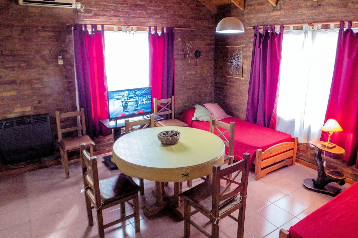 Een gezellige kamer met een bakstenen muur, een televisie, een bed, een tafel en stoelen.