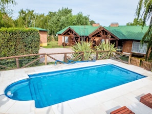 A swimming pool with a wooden deck, surrounded by a wooden fence and a hedge. - Cabañas Rumel (Sierra de la Ventana)