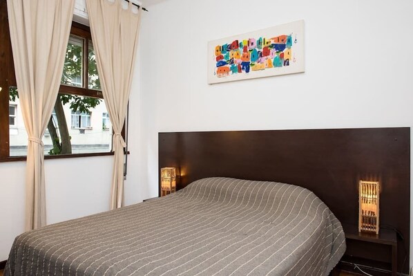A bedroom with a bed, a window with curtains, a wall-mounted artwork, and bedside lamps.