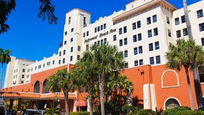 A multi-story hotel with a red and white facade, palm trees in front, and a clear blue sky.