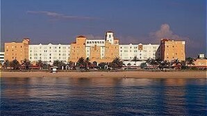 A coastal hotel with multiple buildings, a beach in the foreground, and a calm sea.