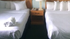 A hotel room with two beds, a nightstand with a lamp, and two framed pictures on the wall.
