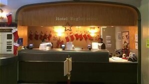 A hotel registration desk with a wooden counter, a sign above it, and Christmas stockings hanging on the wall.