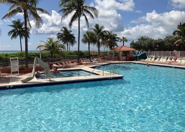A pool with clear water, surrounded by palm trees and lounge chairs.