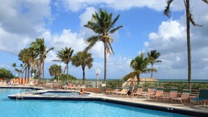A pool area with lounge chairs and palm trees, overlooking a body of water.