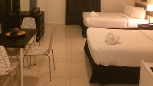 Ein Hotelzimmer mit zwei Betten, einem Schreibtisch, einem Stuhl, einem Spiegel und einem Fenster mit Vorhängen.