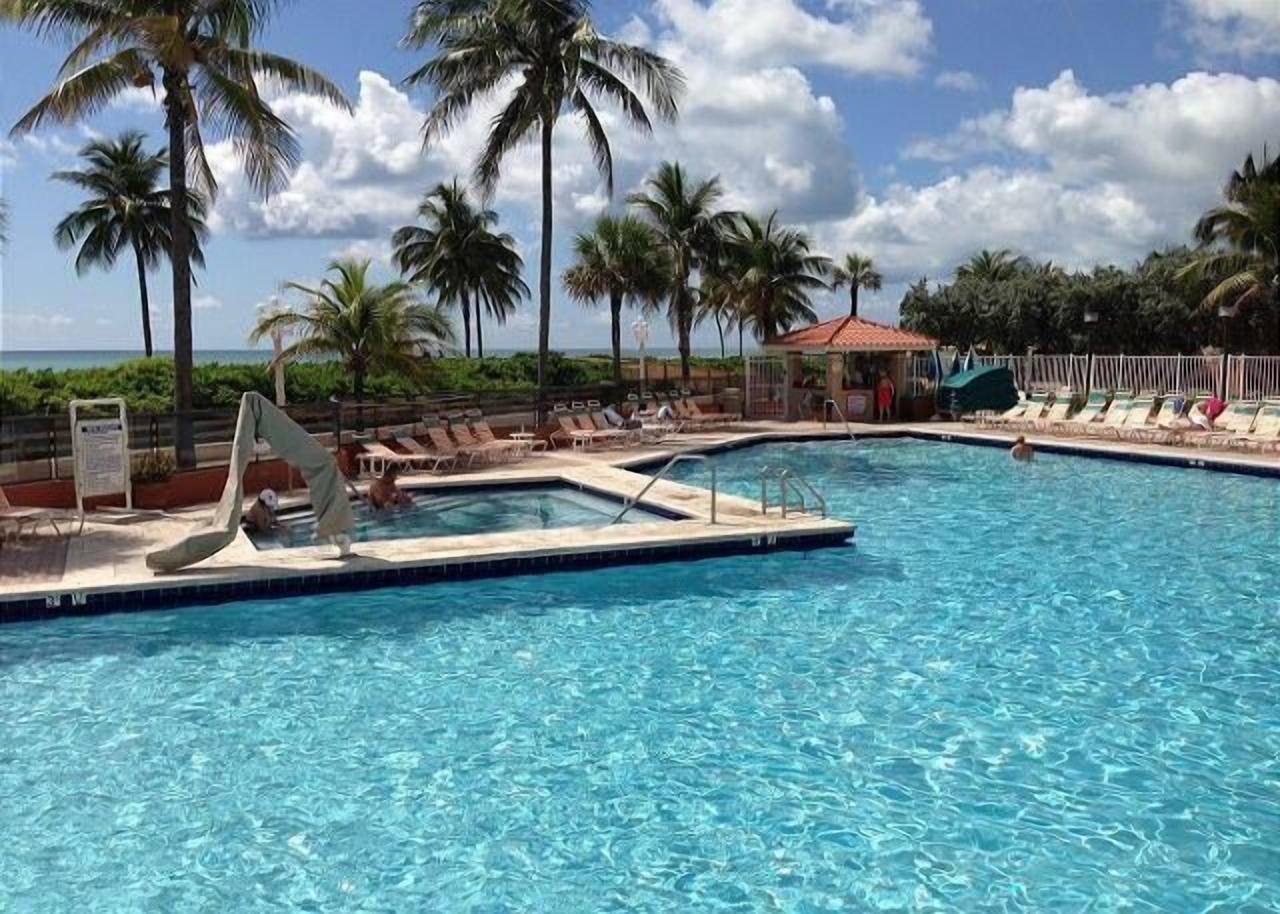 A pool with clear water, surrounded by palm trees and lounge chairs.