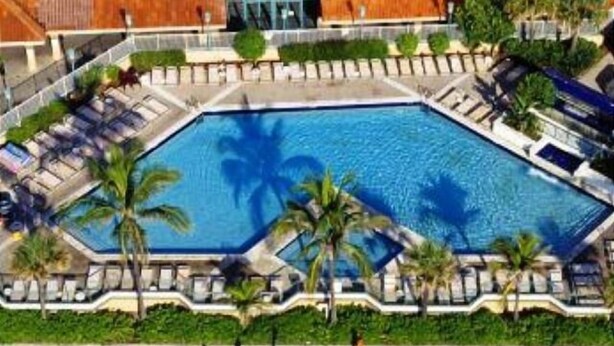 Uma área de piscina com formato geométrico, rodeada por palmeiras e espreguiçadeiras.