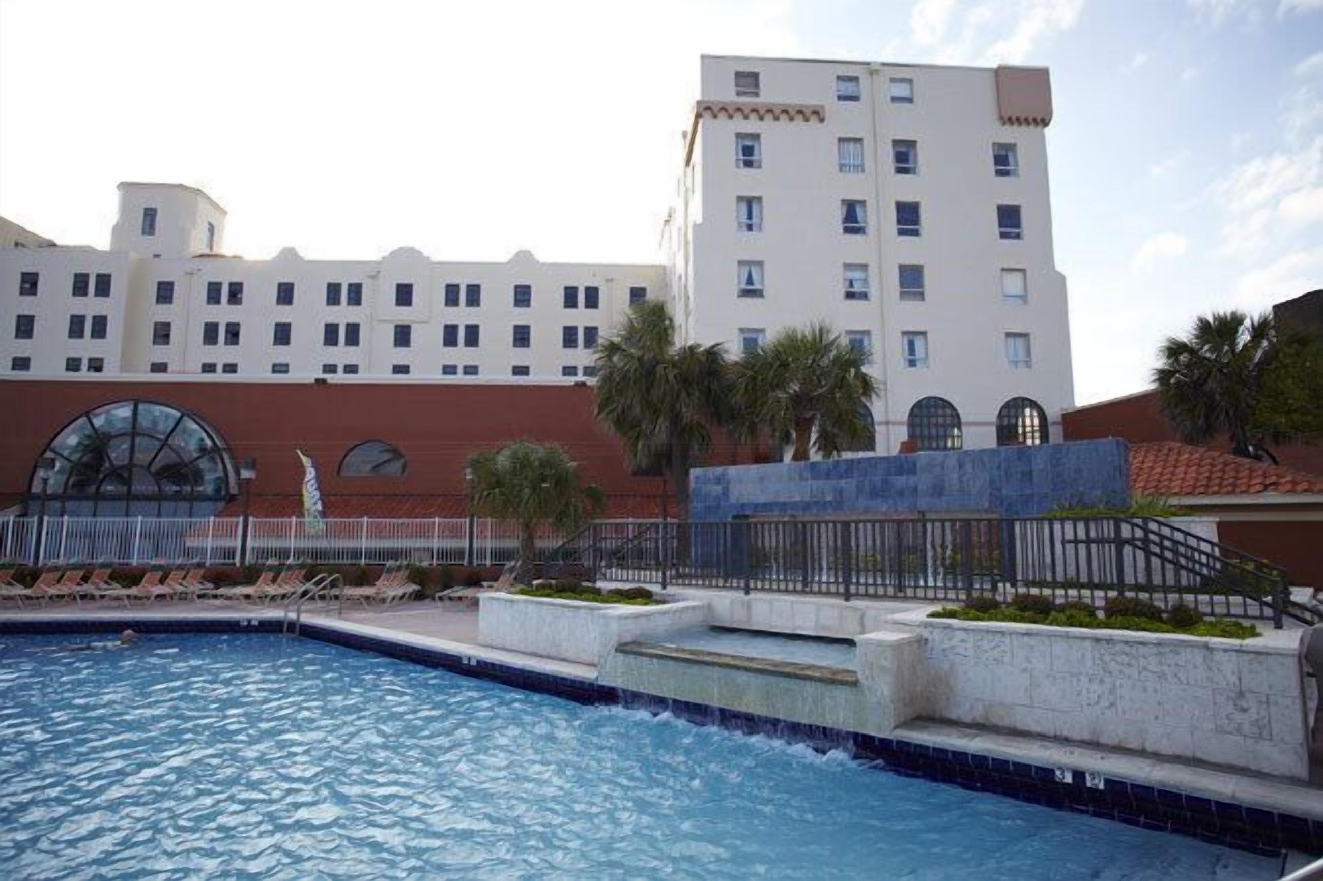 A hotel with a swimming pool, palm trees, and a large building with multiple windows.