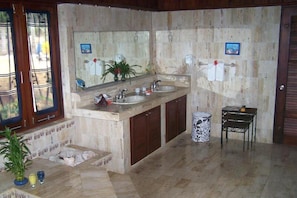 Un baño con dos lavamanos, un espejo grande y una mesita con un florero.