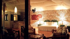 A cozy room with a stone wall, a bed with white linens, and a fan on the wall. - Villa Cabino (Cabrera)
