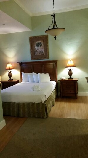 Une chambre d’hôtel avec un grand lit, deux tables de chevet avec des lampes, une tête de lit en bois et un tableau au mur.