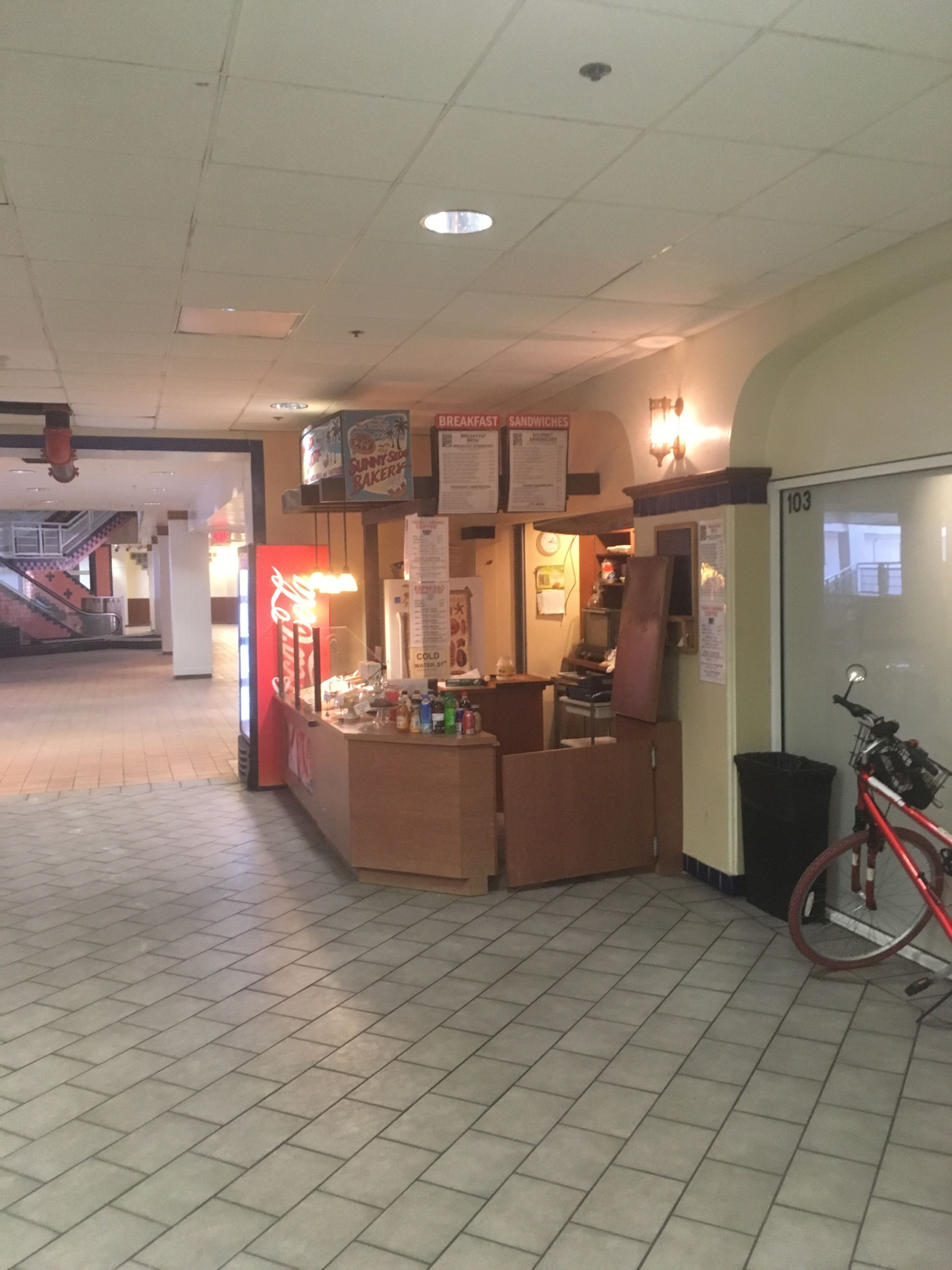 A food kiosk with a menu board, a bicycle parked nearby, and a tiled floor.