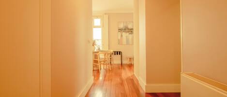 A hallway with wooden flooring, a dining area with a table and chairs, and a painting on the wall.