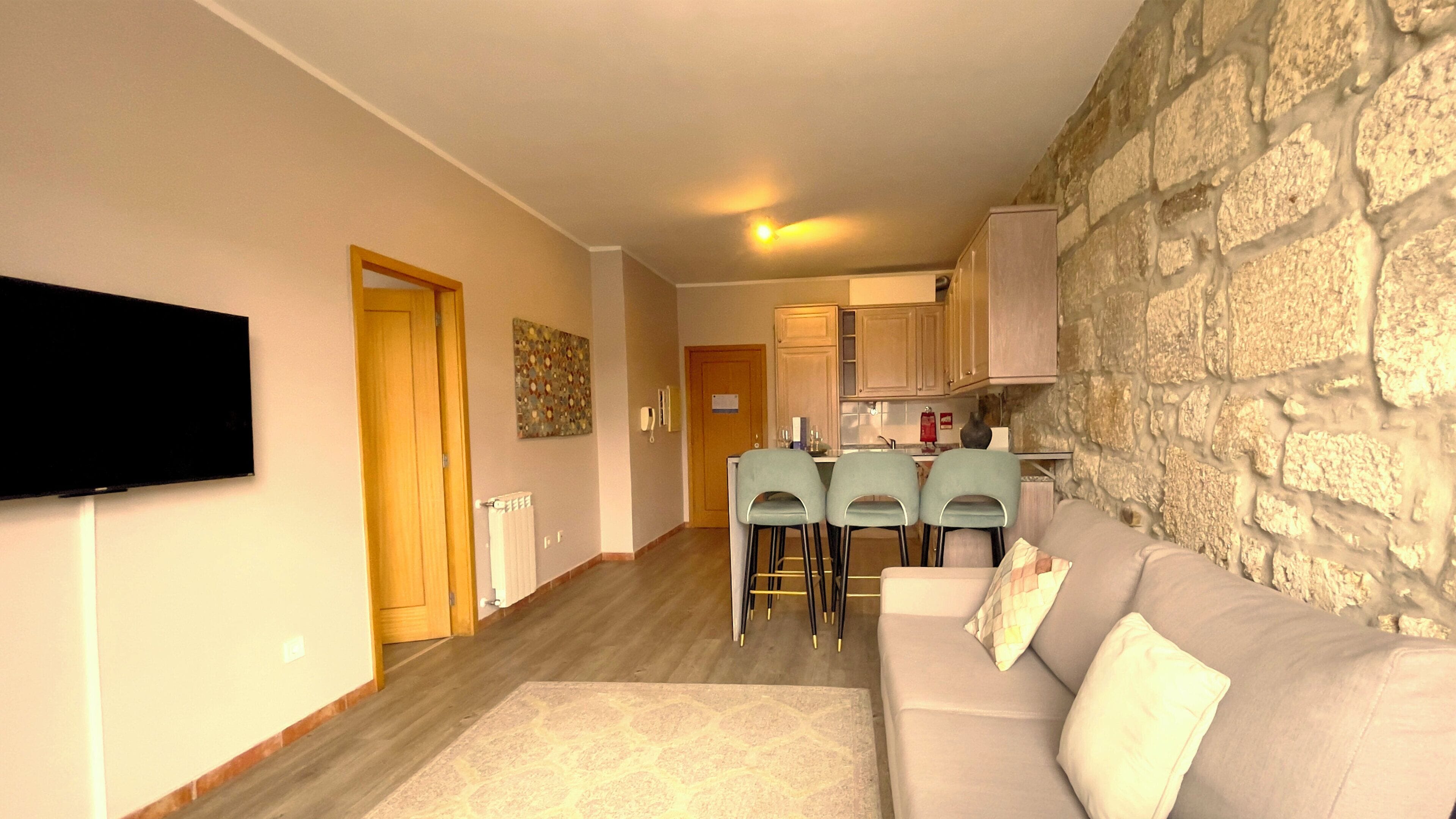 Una sala de estar con sofá, televisor y pared de piedra.
