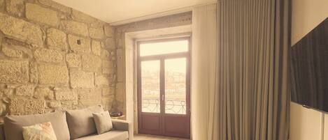 A room with a stone wall, a sofa with cushions, a window with curtains, and a flat-screen TV mounted on the wall.