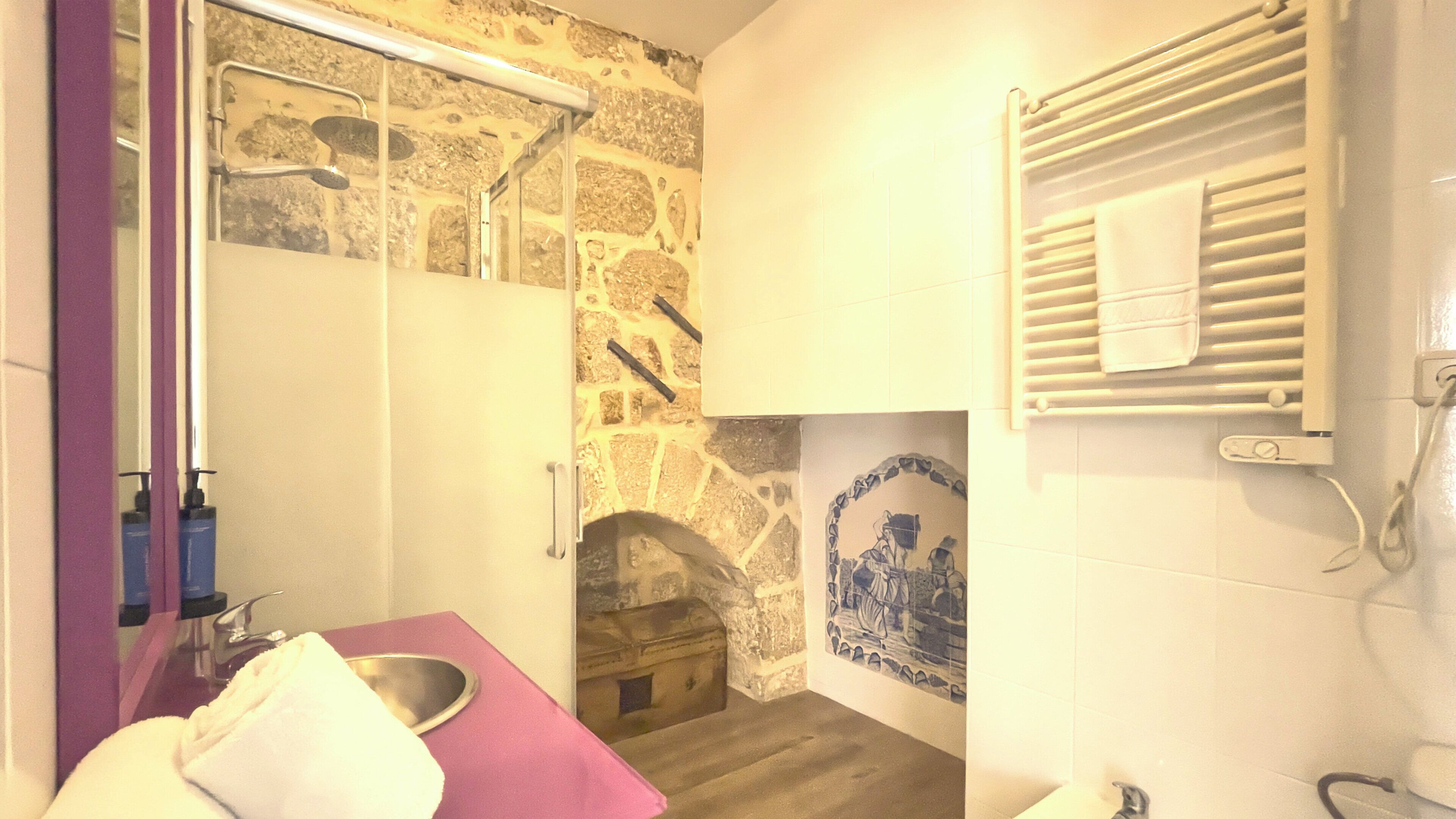 A bathroom with a stone wall, a wooden floor, a sink with a pink towel, a mirror, and a shower with a white towel.