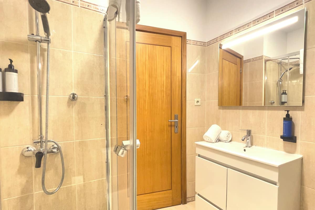 A bathroom with a shower, a sink, a mirror, and toiletries on shelves.