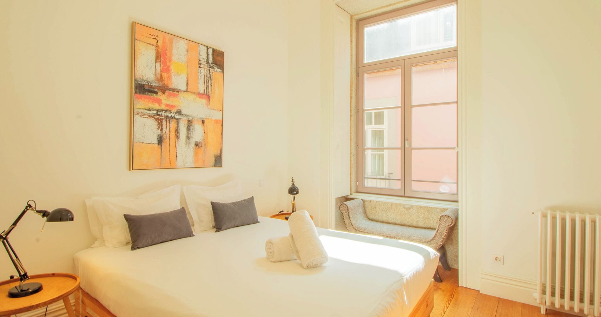A bedroom with a large bed, a window with a view, a radiator, and a painting on the wall.