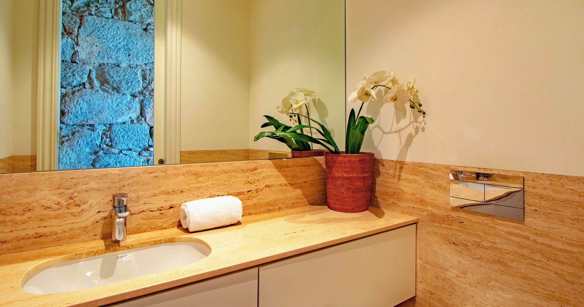 A bathroom with a marble countertop, a sink, a mirror, and two potted orchids.