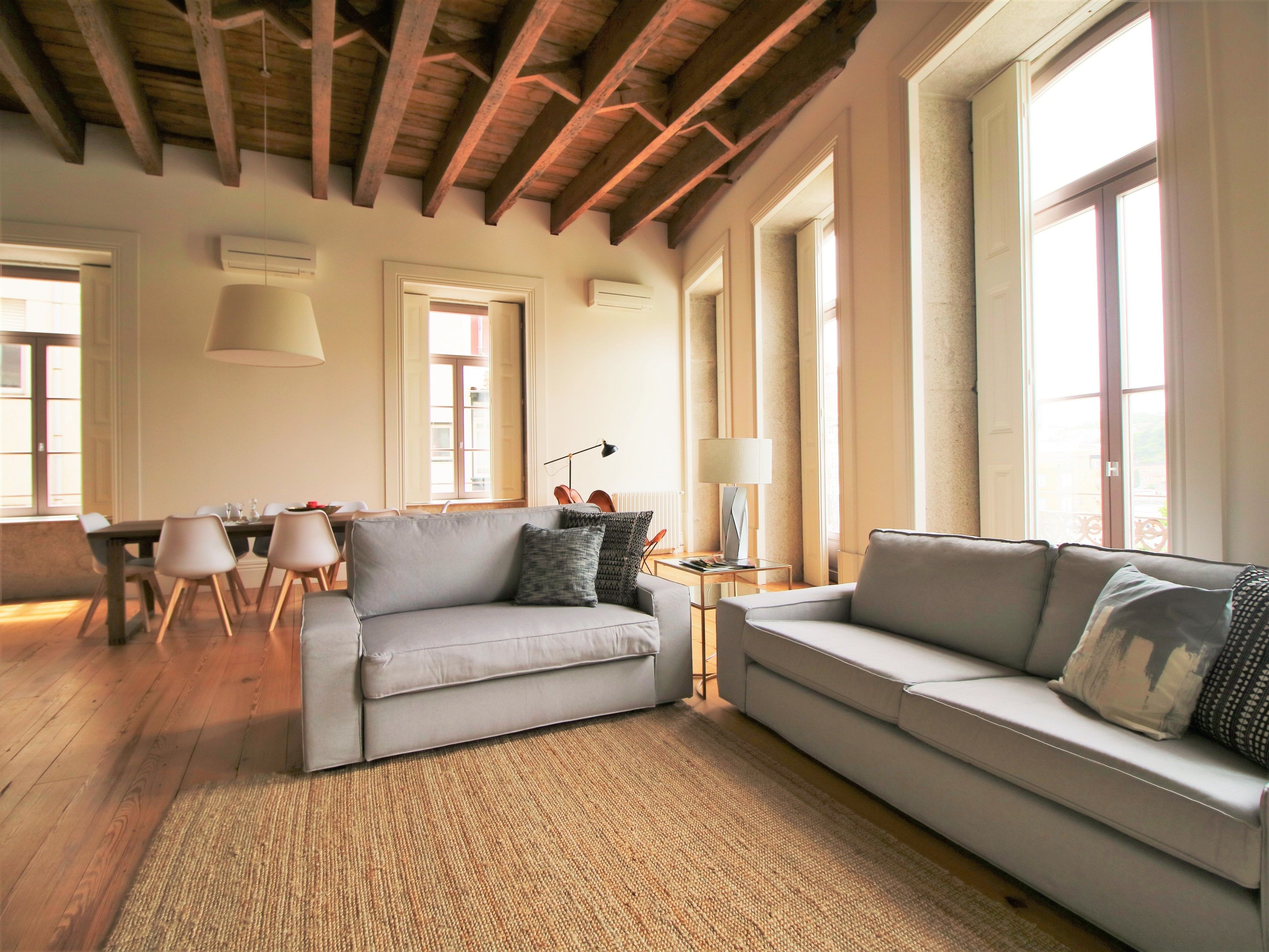 Un ampio soggiorno con soffitto alto, grandi finestre e un'area pranzo con tavolo e sedie.